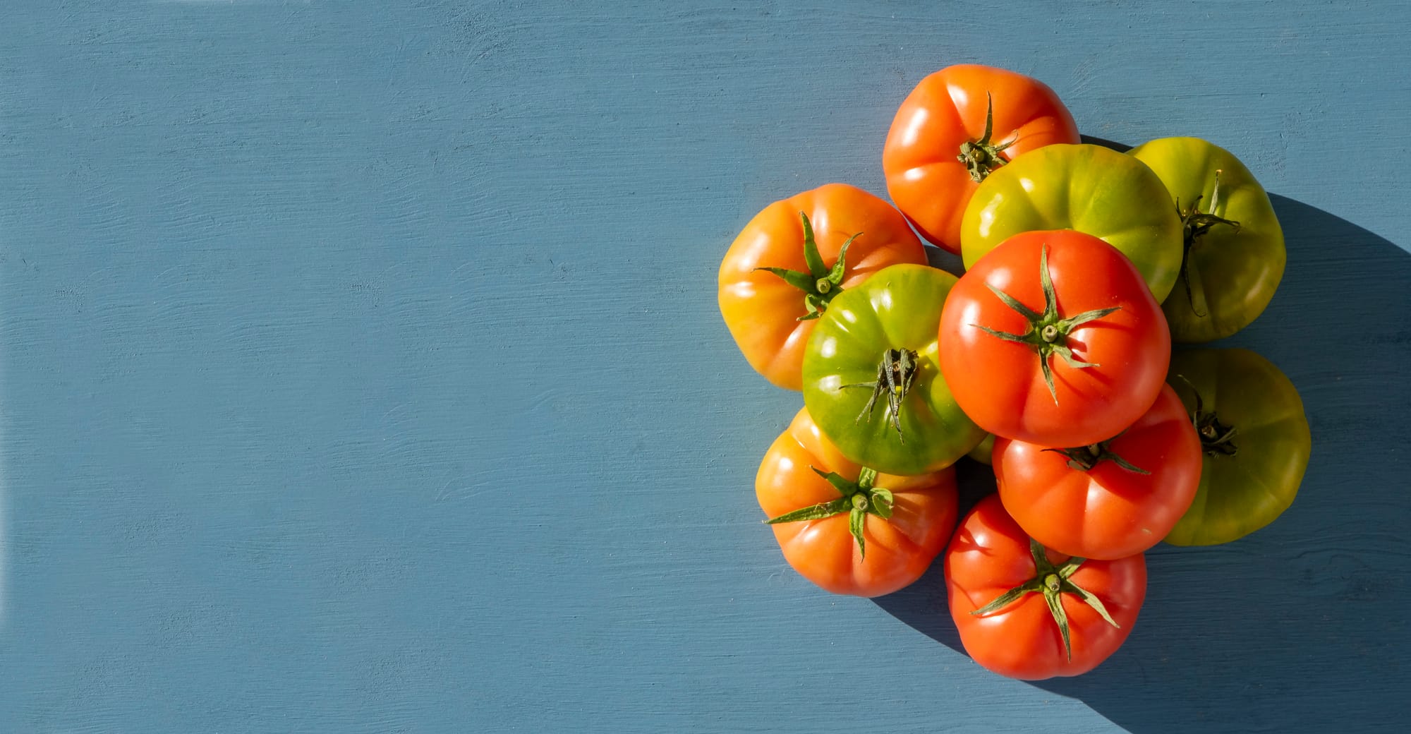 An aerial view of a stack of heirloom tomatoes on a painted blue background 